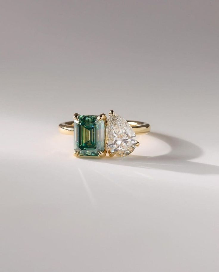 an emerald and diamond ring with two pear shaped diamonds on the side, set in yellow gold