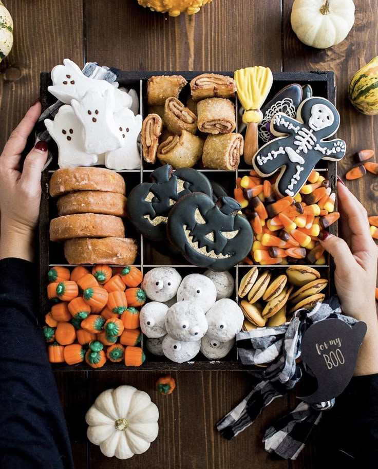 a person holding a tray filled with halloween cookies and other treats on top of a wooden table