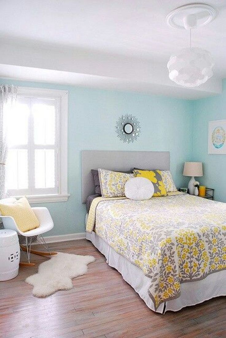 a bedroom with light blue walls and wood flooring, white bedding and yellow accents