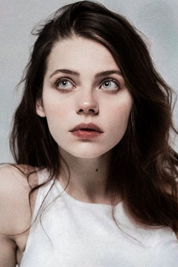 a woman with long brown hair wearing a white tank top and looking at the camera