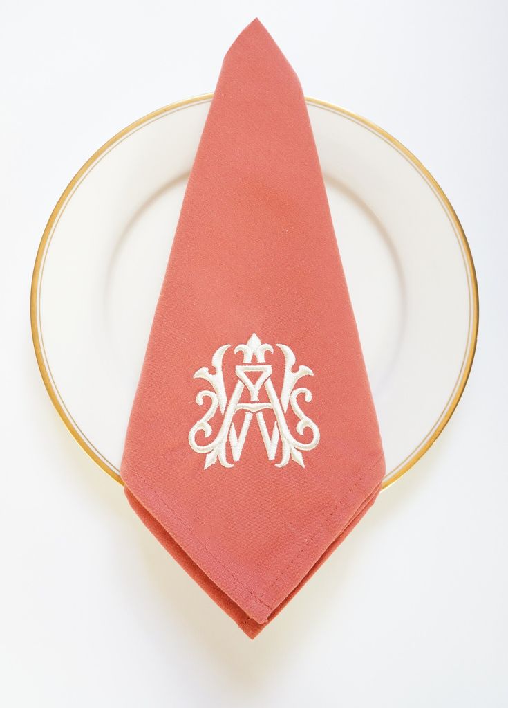 a red napkin on a white plate with a monogrammed initial in the middle