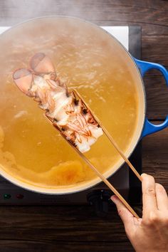 a person holding two chopsticks over a pot of food