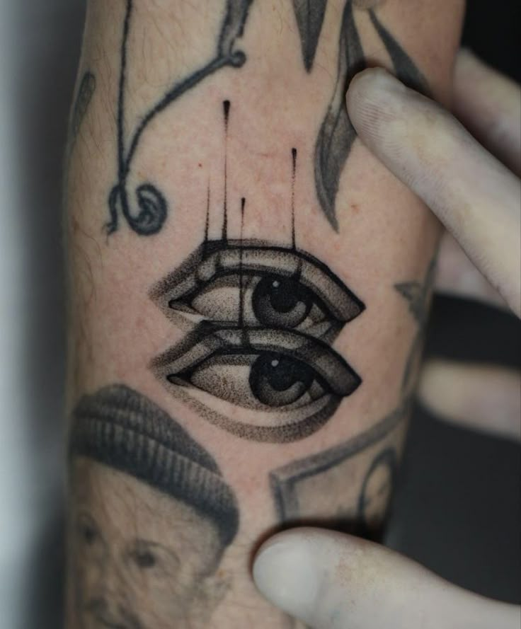 a hand holding up a tattoo with an eye and other tattoos on the arm behind it