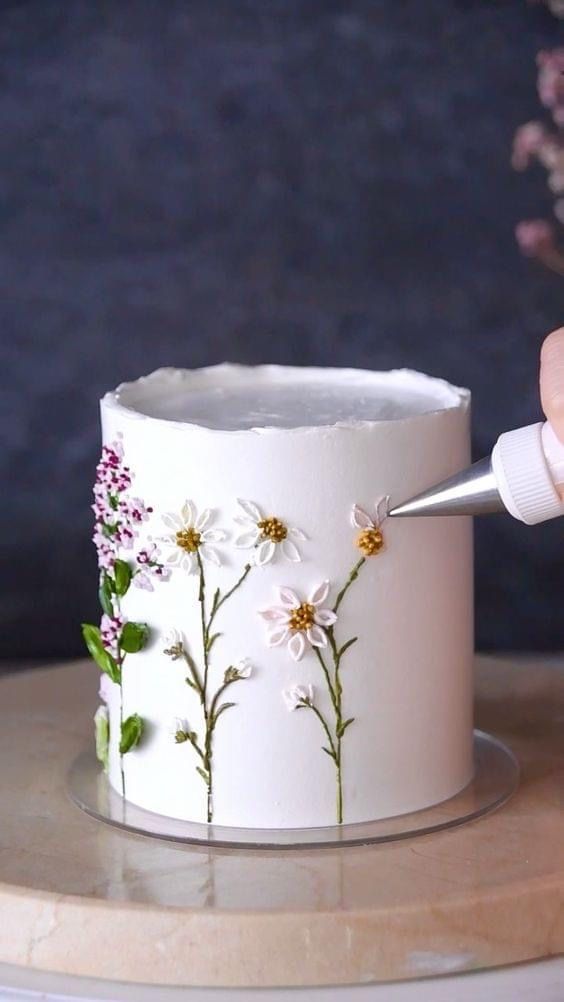 someone is decorating a white cake with flowers on it and the icing has been applied