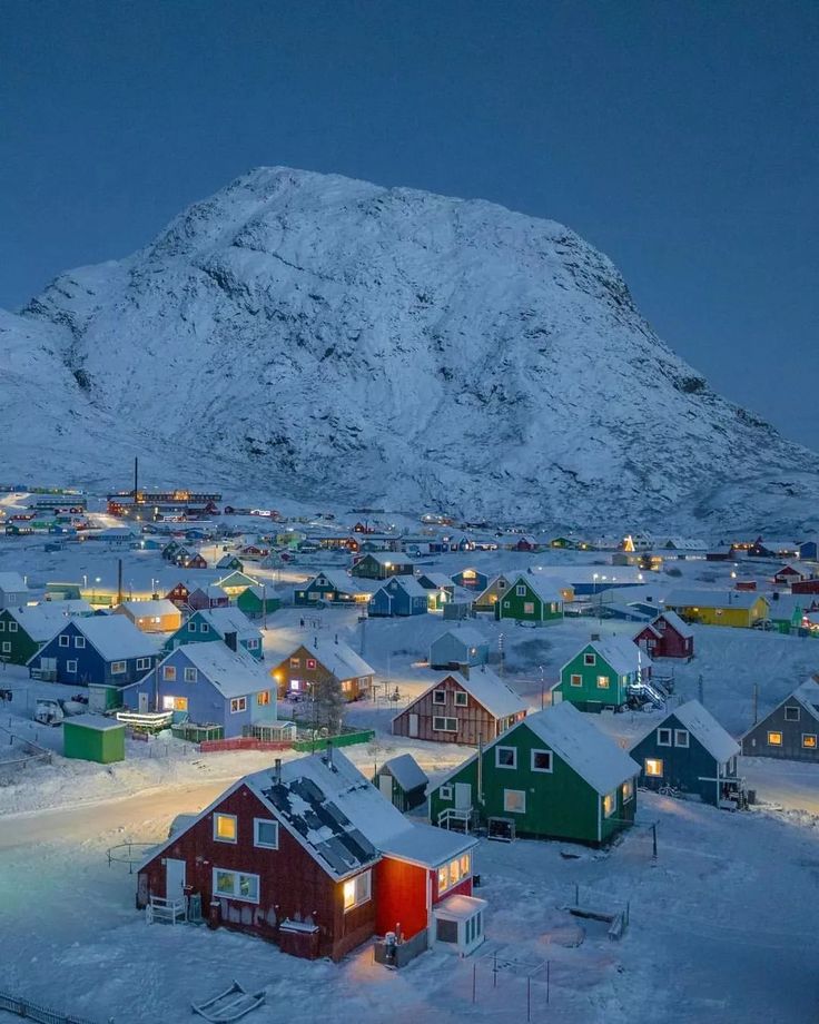 a small town in the middle of a snowy field with mountains in the background at night