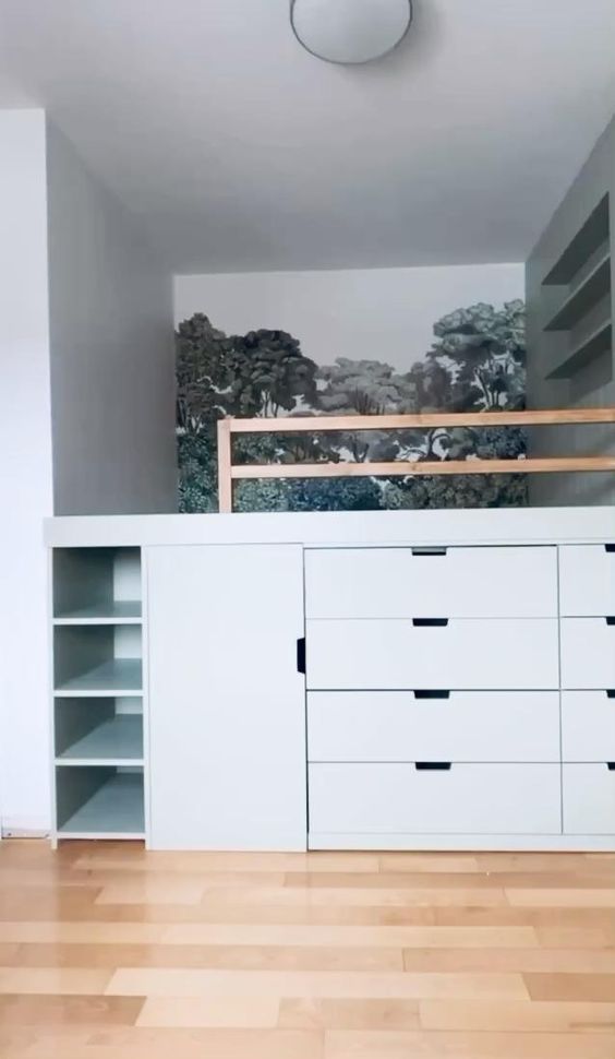 an empty room with white drawers and shelves on the wall, next to a bed