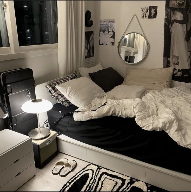 an unmade bed sitting in a bedroom next to a dresser and window with pictures on the wall