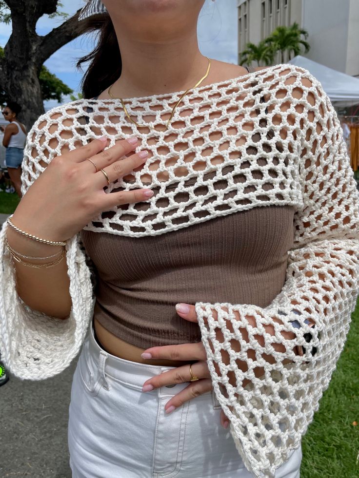 a woman with her hands on her chest wearing a crochet top and white pants