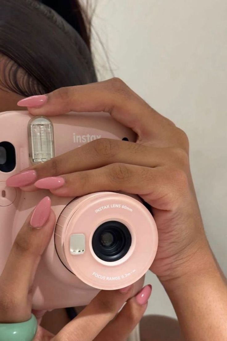 a woman is taking a photo with her pink instax camera in front of her face