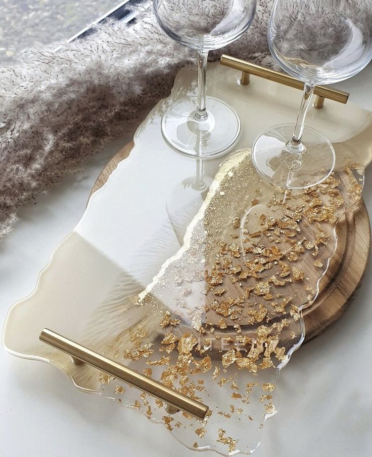 two wine glasses sitting on top of a wooden tray with gold flakes in it