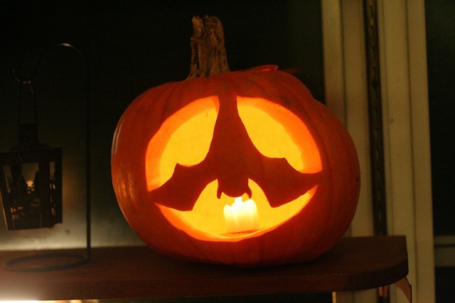 a carved pumpkin sitting on top of a shelf with a lit candle in the shape of a bat