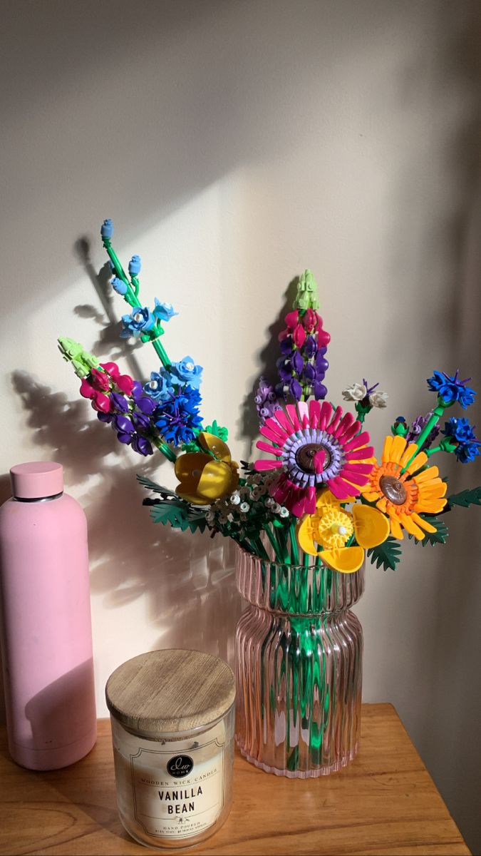 a vase filled with colorful flowers next to a pink container on a wooden counter top