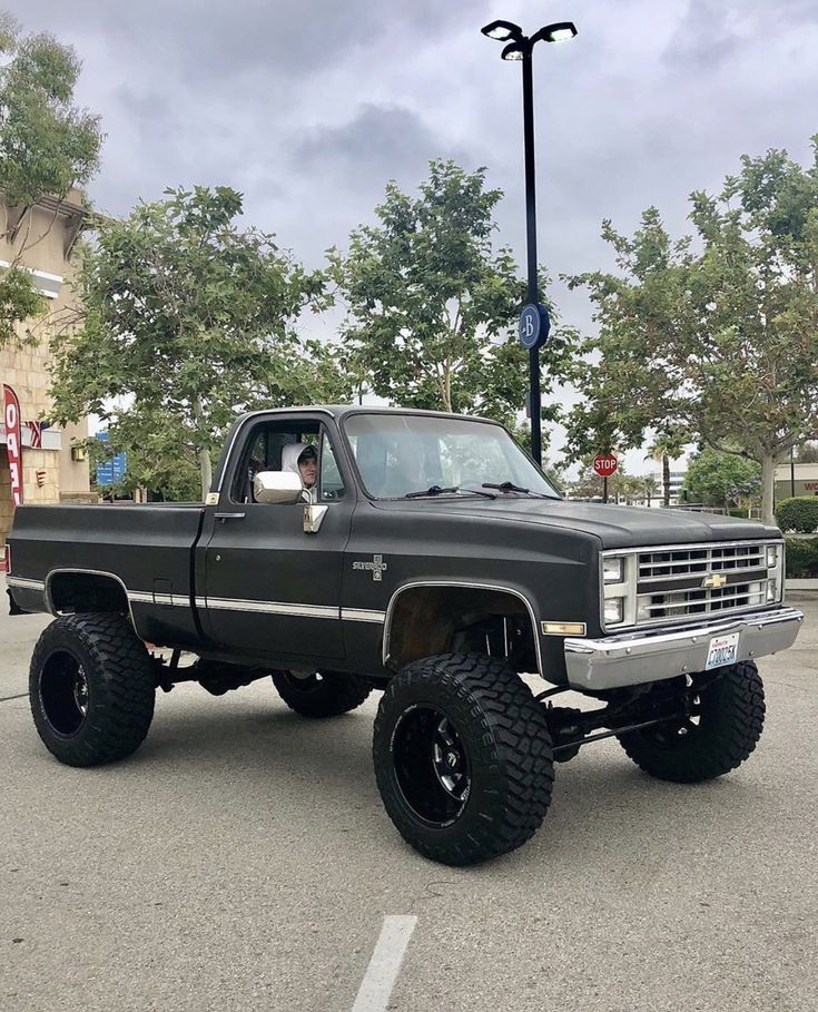 a large black truck parked in a parking lot next to a street light and trees