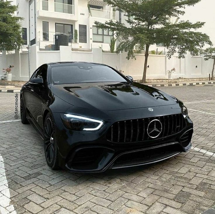 a black car parked in front of a building on a brick road next to trees