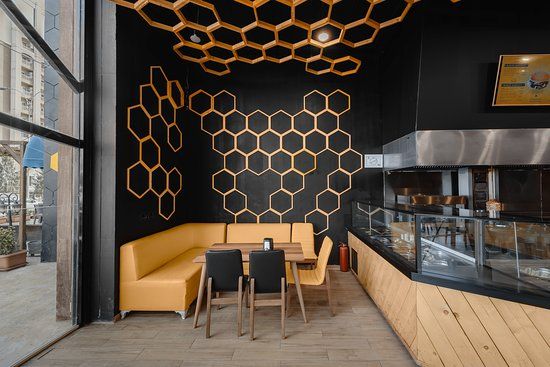 the interior of a restaurant with black walls and wooden tables, yellow chairs and honeycombs hanging from the ceiling