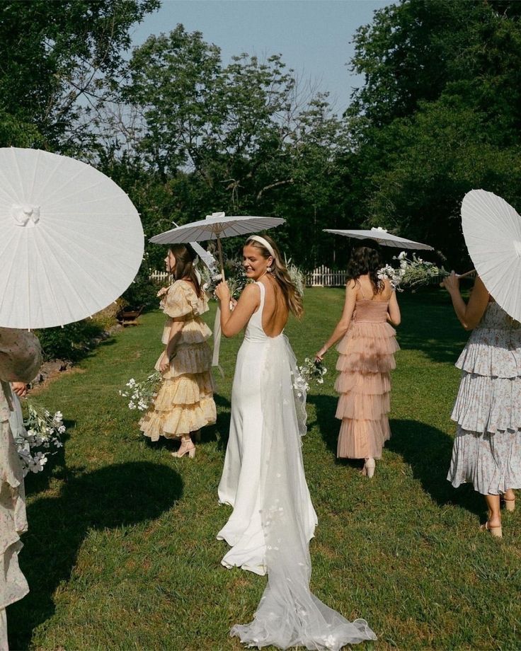 a group of women standing on top of a lush green field holding white umbrellas