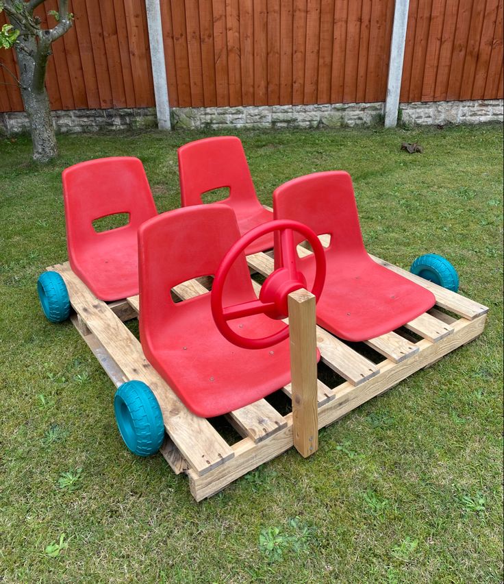 two red chairs sitting on top of a wooden pallet in the middle of a yard