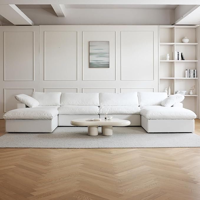 a large white couch sitting on top of a wooden floor next to a book shelf