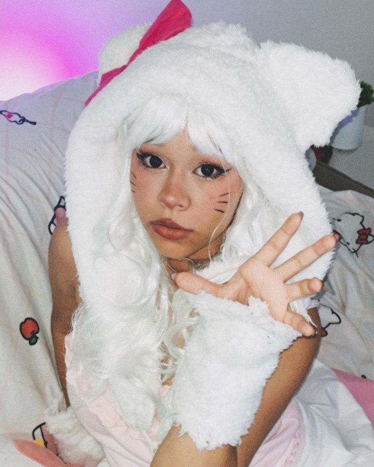 a woman with white hair is wearing a furry hat and holding her hand up to the camera