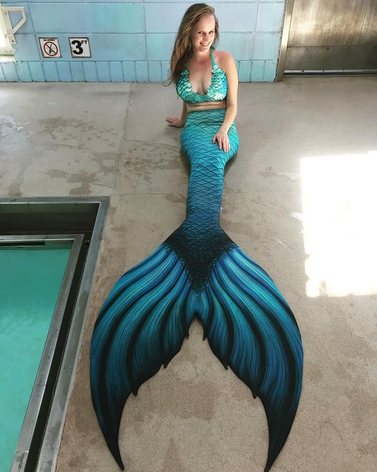 a woman is sitting on the floor in front of a fake mermaid tail that has been painted blue and green