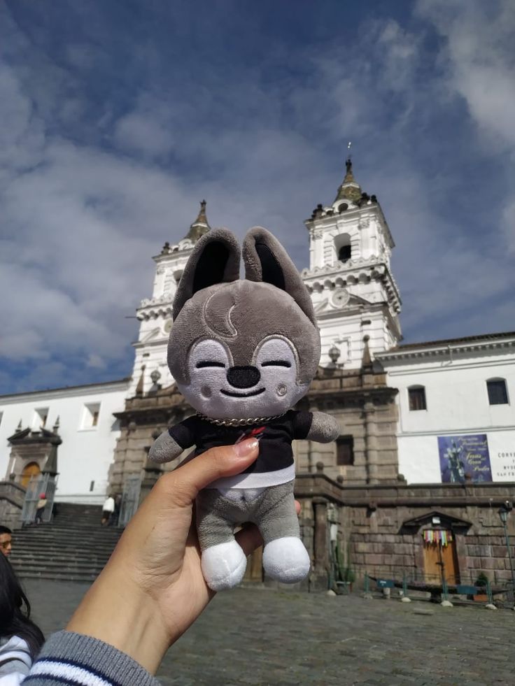 a person holding up a stuffed animal in front of a building with a clock tower