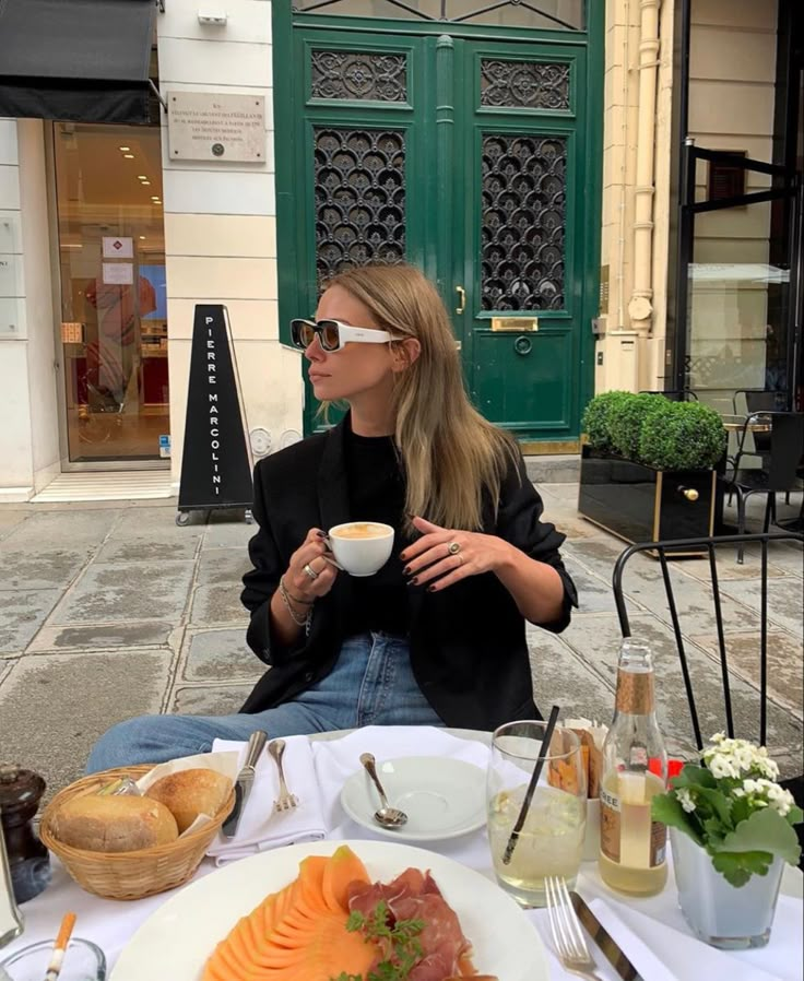 a woman sitting at a table with food and drinks in front of her on the street