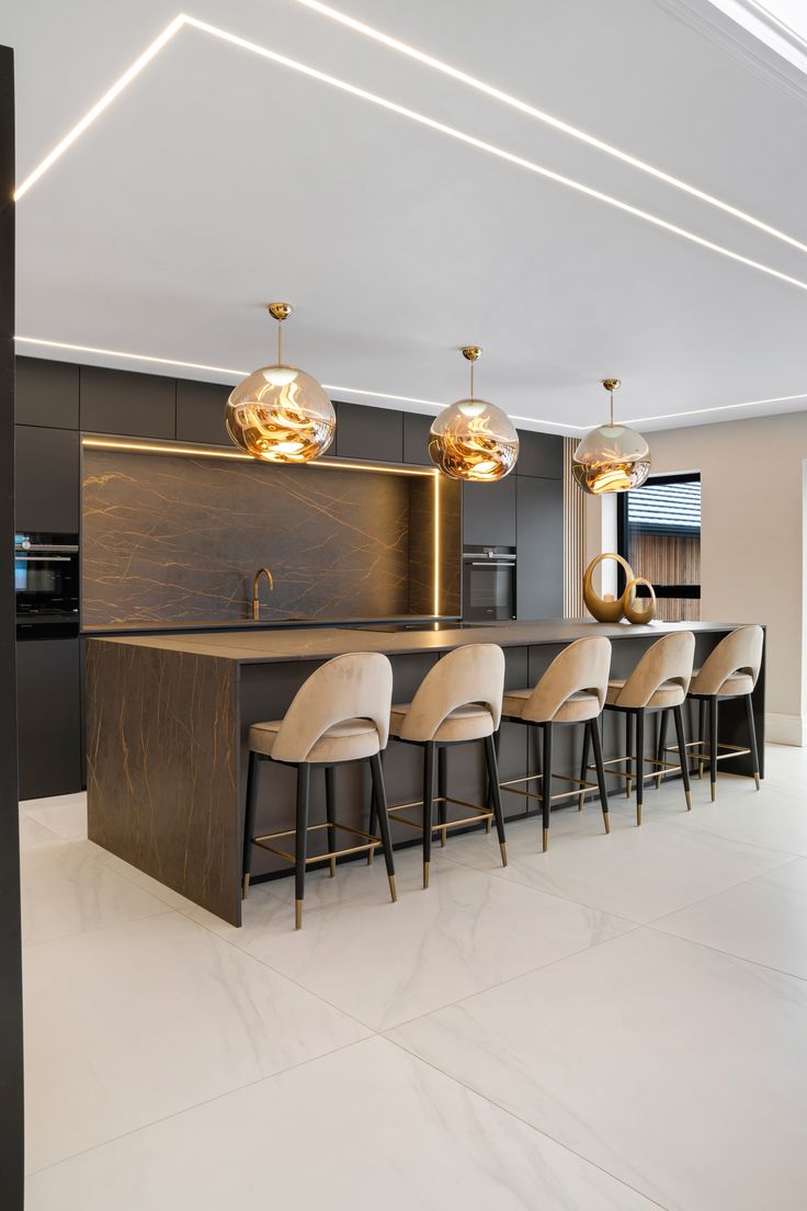 a modern kitchen with marble counter tops and bar stools, along with gold pendant lights