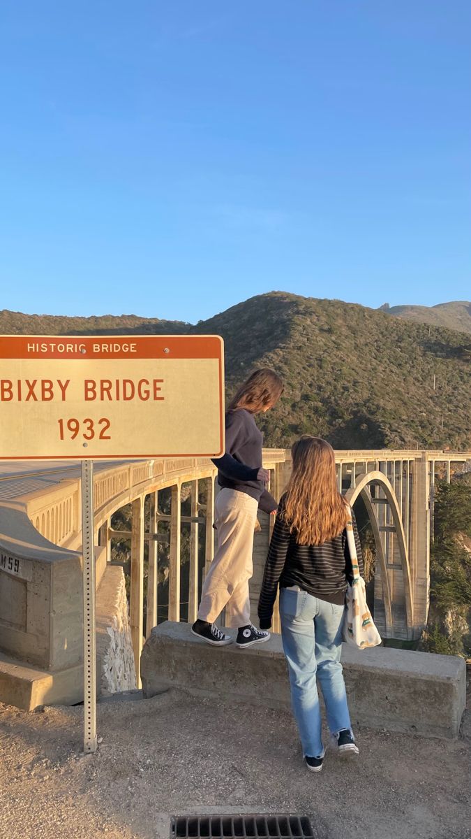 two people standing on the side of a bridge next to a sign that says bixby bridge 1932