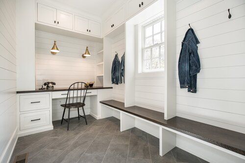 a kitchen with white walls and wood flooring next to a wooden bench in front of a window