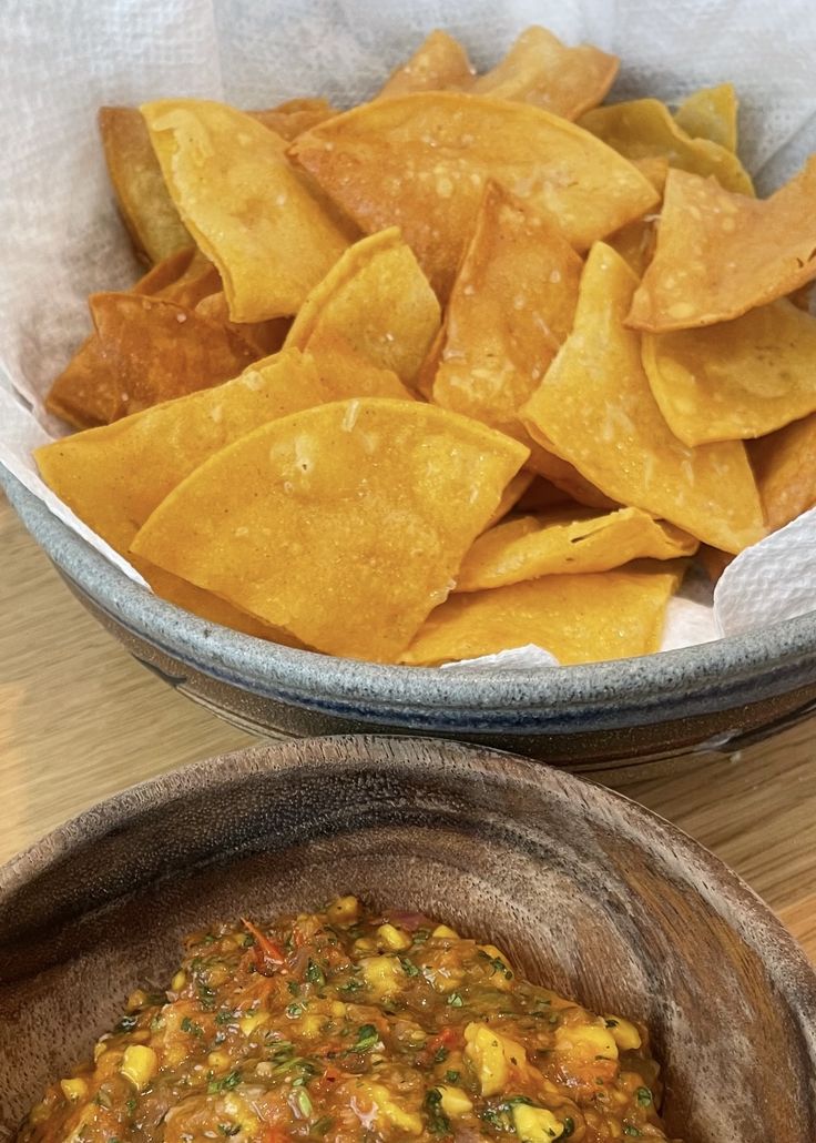 two bowls filled with chips and salsa on top of a wooden table