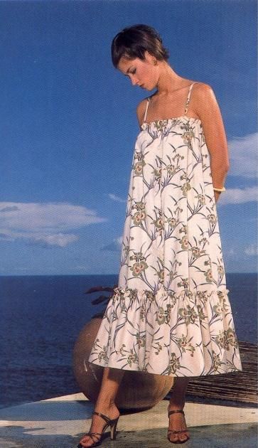 a woman in a white dress standing on the edge of a pier looking down at the water