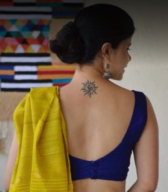 a woman wearing a blue and yellow sari with a sun tattoo on her back