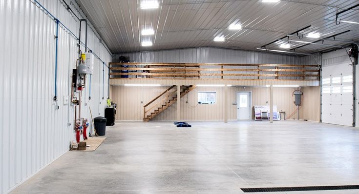 an empty warehouse with white walls and metal stairs leading up to the second floor area