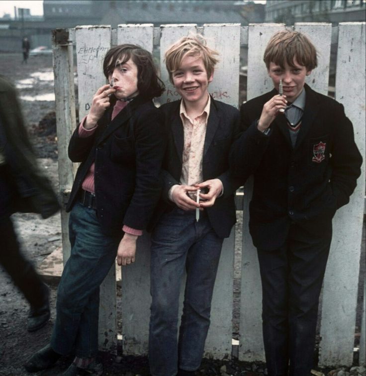 three young men standing next to each other in front of a wooden fence eating food