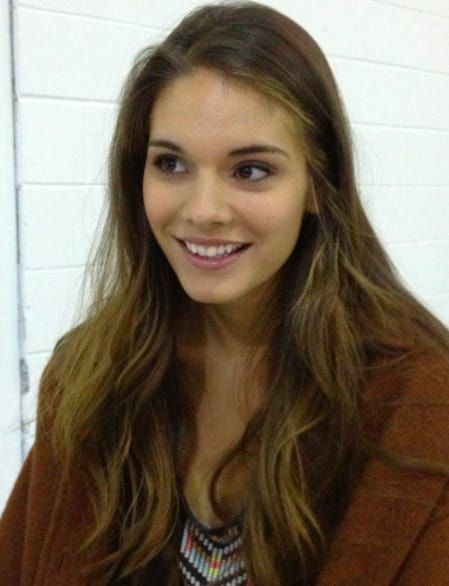 a woman with long hair is smiling and wearing a brown jacket over a black shirt