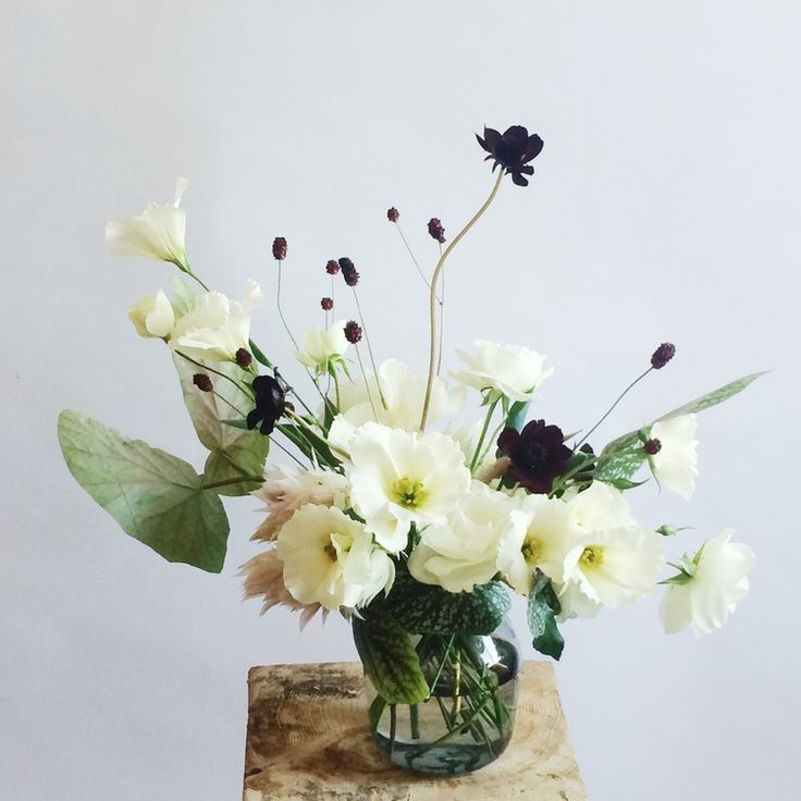 a vase filled with white and black flowers on top of a piece of drift wood