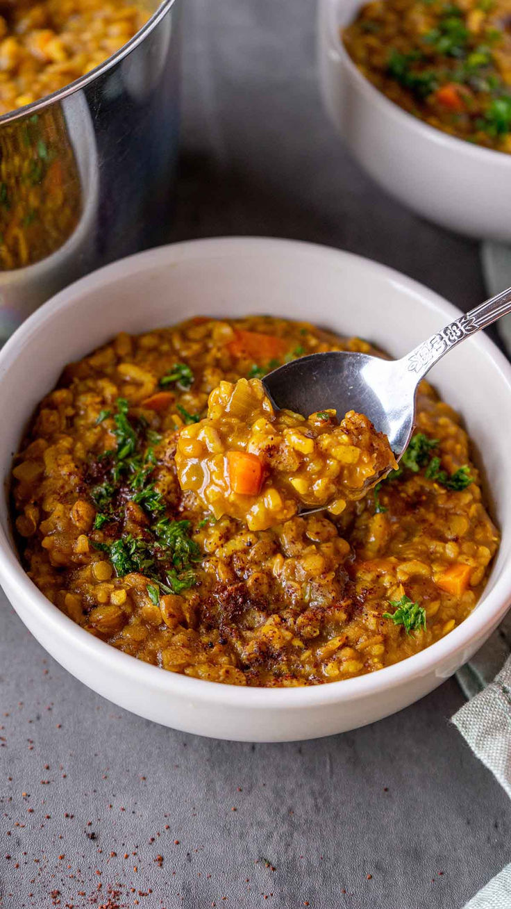 a white bowl filled with food next to two silver pans full of soup and one has a spoon in it