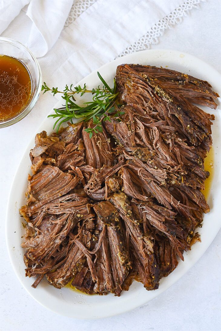 a white plate topped with sliced meat next to a glass of beer and napkins