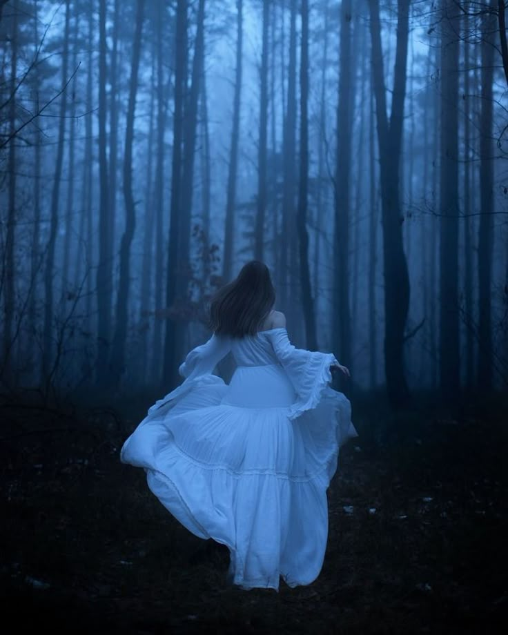 a woman in a white dress is walking through the woods with her arms spread out