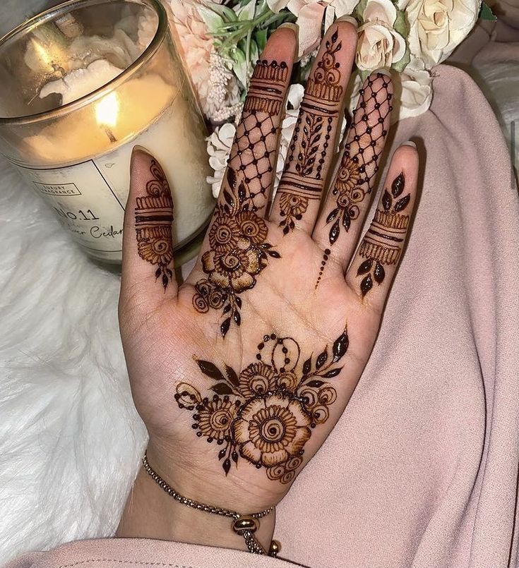 a woman's hand with henna on it next to a candle and flowers