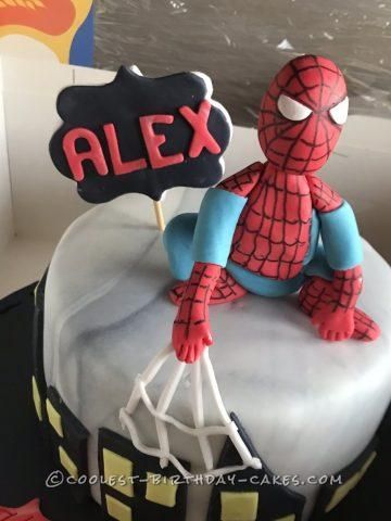 a spiderman cake is sitting on top of a table with a sign that says alex