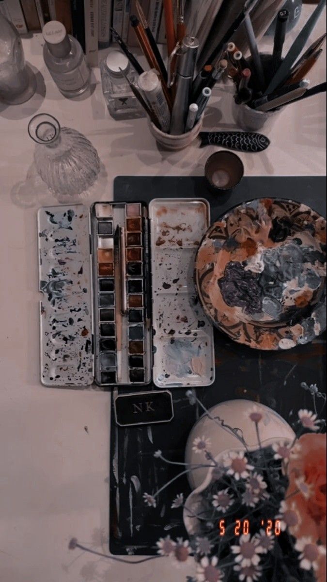 an assortment of art supplies on a table with paintbrushes and other items in the background