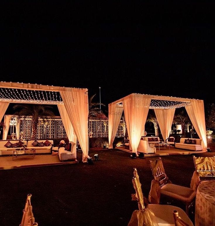 an outdoor wedding setup at night with white drapes and lights on the canopy over the seating area