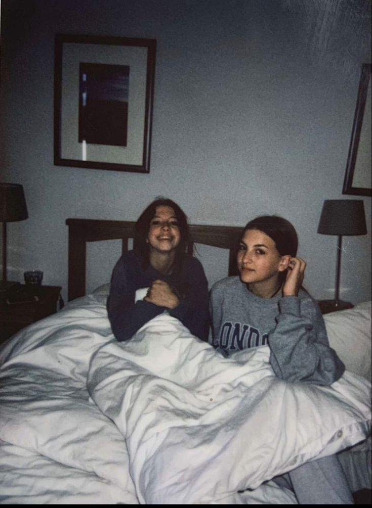 two women sitting on a bed with white sheets