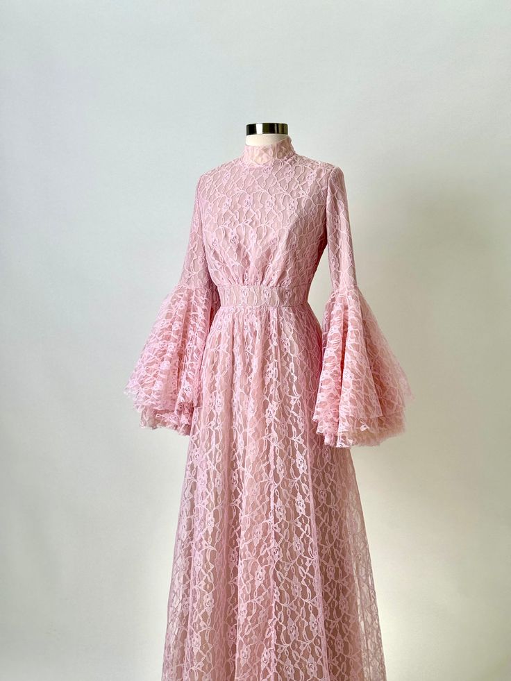 Revel in the romantic allure of this Anna Augusta Evening Maxi Dress, designed in a delicate pink lace that conjures visions of elegance and femininity. This pre-worn size 8 gown is in perfect condition, featuring a full-length lace overlay that provides a stunning visual texture. The dress is accented with dramatic bell sleeves and a cinched waist, enhancing the silhouette and providing a timeless charm ideal for formal occasions, elegant receptions, and bridal parties. Pristine Condition: Carefully preserved to maintain a flawless appearance. Delicate Pink Lace: Soft and feminine, perfect for elegant affairs. Dramatic Bell Sleeves: Add a touch of vintage elegance and dramatic flair. Flattering Cinched Waist: Highlights the silhouette beautifully. Suitable for Various Formal Events: Ideal Elegant Pink Lace Dress For Wedding, Elegant Pink Lace Wedding Dress, Elegant Pink Lace Evening Dress, Pink Long Sleeve Lace Dress For Evening, Pink Evening Dress With Lace Sleeves, Feminine Pink Dress With Delicate Lace, Pink Spring Lace Dress With Delicate Details, Pink Delicate Lace Dress For Spring, Elegant Pink Lace Dress With Lace Trim