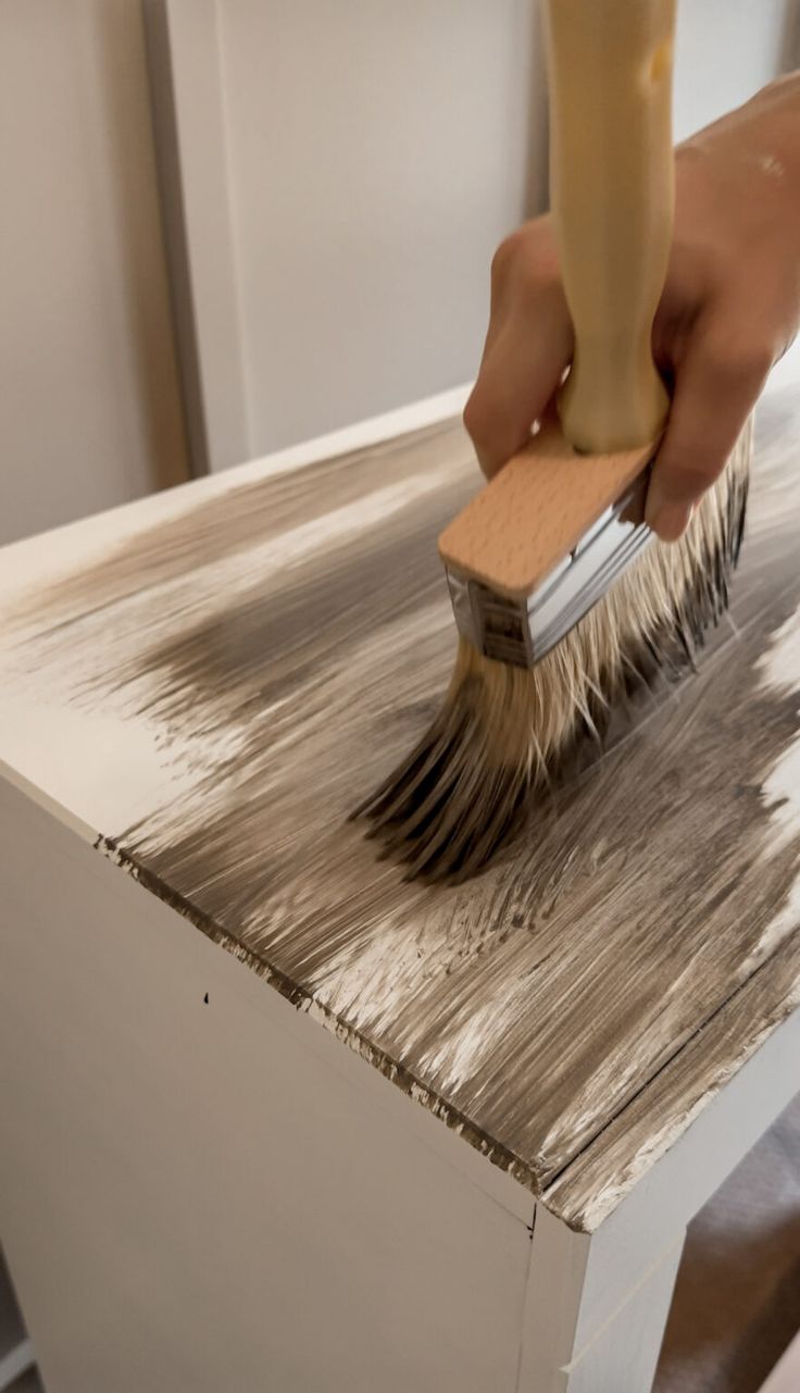 a person with a brush on top of a wooden table that has been painted white