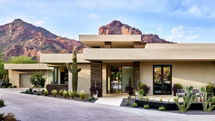 a desert style house with mountains in the backgrouds and cactus trees on either side