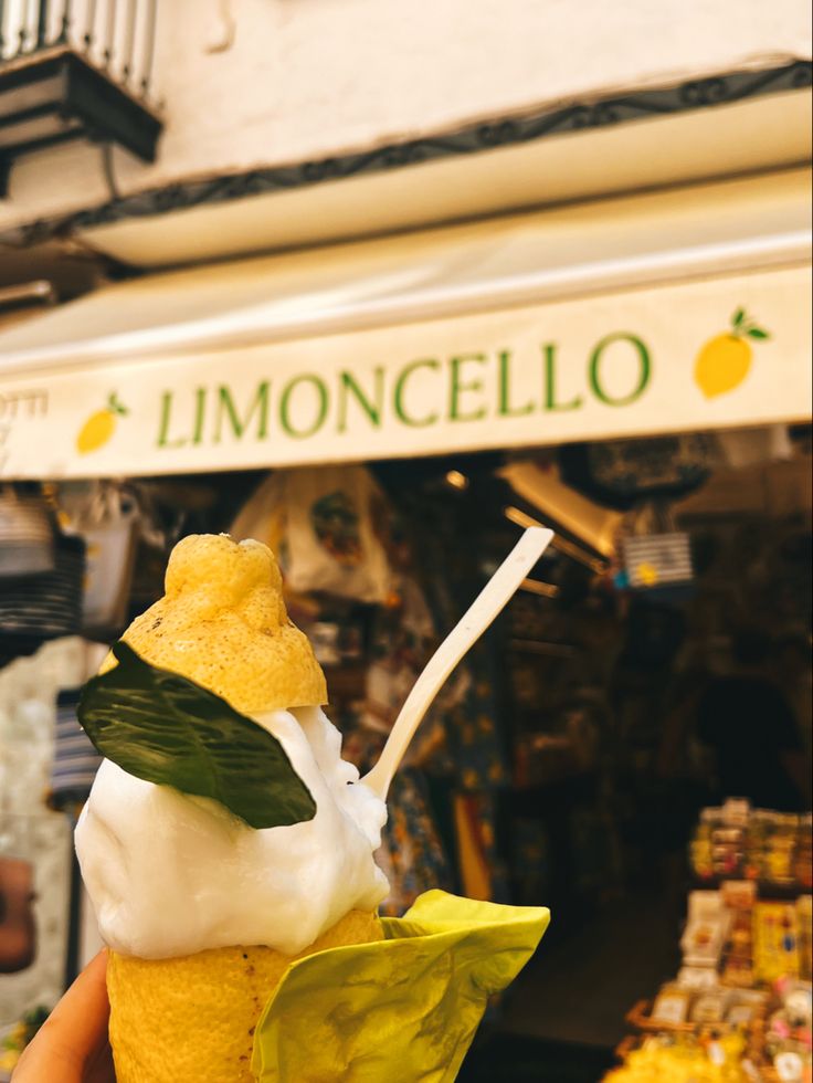 a hand holding an ice cream sundae in front of a lemoncello store