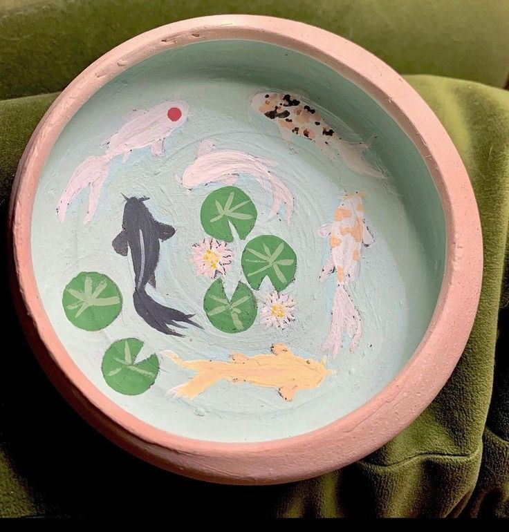 a pink bowl with painted animals and lily pads on the bottom is sitting on a green blanket