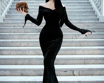 a woman in a long black dress is walking down the stairs holding a purse and looking off into the distance